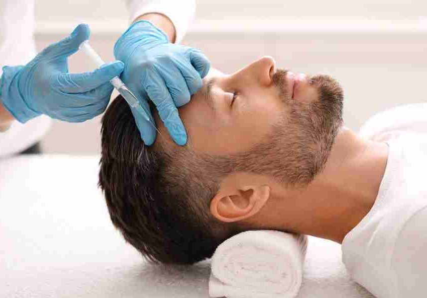 Side view of handsome middle aged man getting hair treatment at beauty salon. Man having mesotherapy session at aesthetic clinic, therapist hands in gloves making injection in scalp, closeup